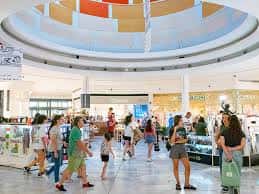 Interior del centro comercial con atrio circular, iluminación natural y personas caminando