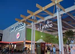 Fachada nocturna del cine Yelmo y zona de ocio 'El Patio' con estructura de madera y luces