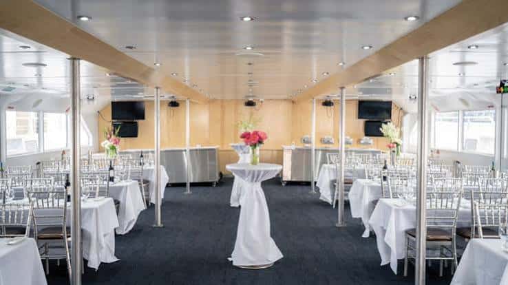 Interior del barco decorado para un evento con mesas, sillas y flores