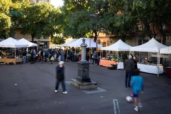 Vista general del Mercat de Pagès a la Plaça de l'Assemblea con puestos bajo carpas blancas y fuente central