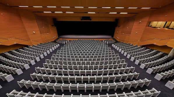 Interior del auditorio principal con butacas grises dispuestas en gradas y escenario oscuro