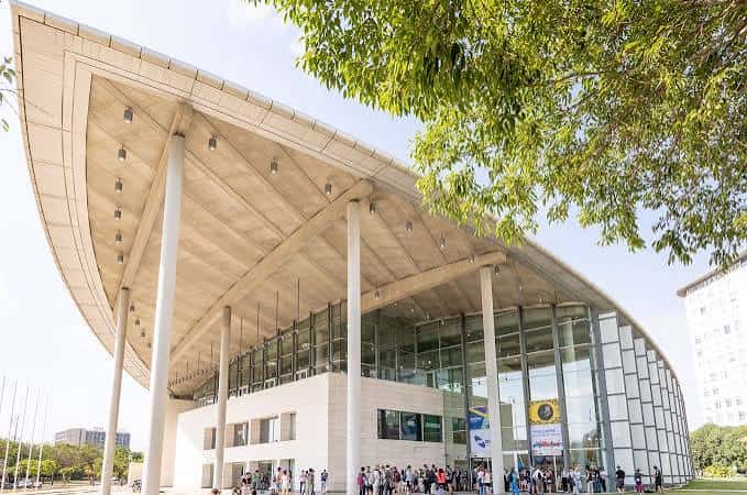Entrada del palacio con personas congregadas y detalle de la estructura arquitectónica bajo árboles