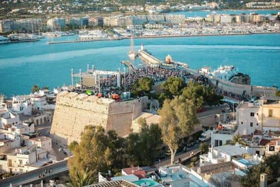 Evento al aire libre en el Baluarte de Santa Lucía con escenario y público junto al puerto de Ibiza