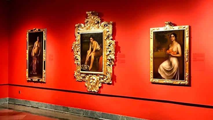Galería interior con tres pinturas destacadas en marcos ornamentados sobre fondo rojo intenso