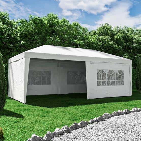 Gran carpa blanca montada en un jardín con césped y árboles al fondo