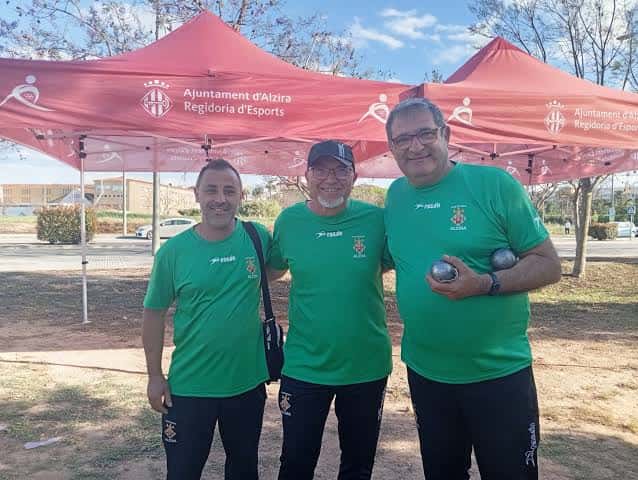 Tres participantes sonrientes con camisetas del club bajo una carpa institucional