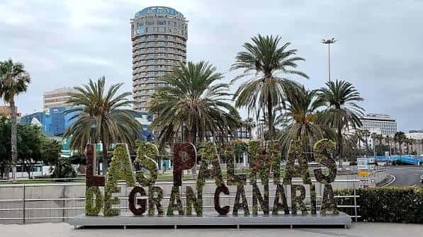 Letrero de Las Palmas de Gran Canaria con palmeras y el edificio de la Torre Espacial al fondo