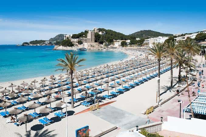 Playa de Palmira con hamacas y palmeras, mostrando su ambiente turístico y amplio paseo marítimo