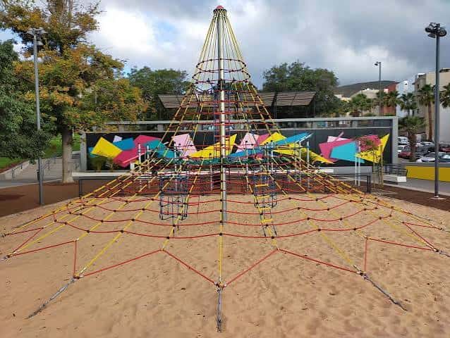 Estructura de escalada en forma de pirámide con redes coloridas sobre arena