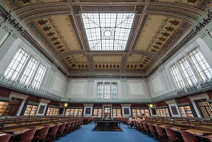 Interior del salón de lectura con techos ornamentados, ventanales y mesas de estudio