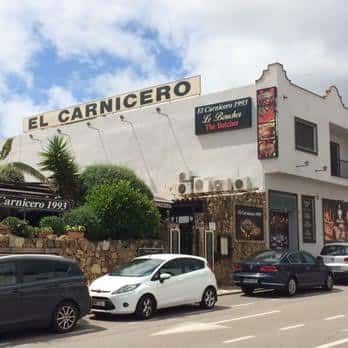 Fachada del restaurante El Carnicero 1993 en Estepona con letrero visible y vehículos estacionados frente al local