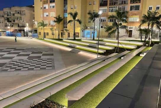 Vista nocturna de la plaza iluminada, mostrando el diseño de los bancos y la vegetación