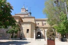 Fachada principal de la Iglesia de San Juan Bautista con entrada arqueada y campanario bajo el cielo azul