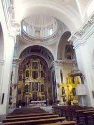 Interior de la iglesia con altar barroco dorado, bóveda central y bancos de madera dispuestos para ceremonias