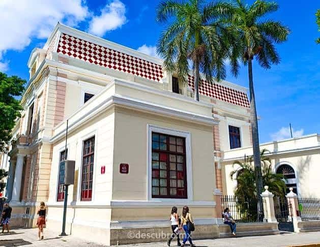 Fachada principal del museo con palmeras y detalles arquitectónicos en tonos crema y rojo