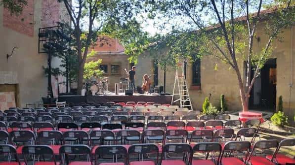 Vista general del patio exterior con escenario y sillas dispuestas para evento
