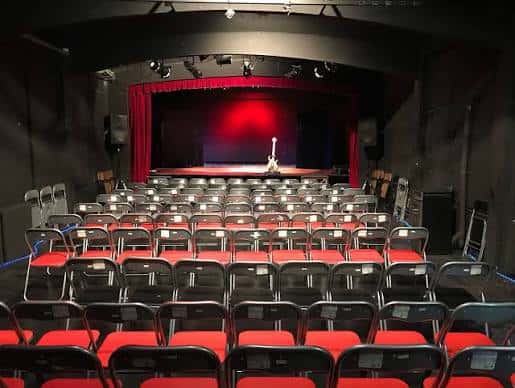 Interior del auditorio con escenario, cortinas rojas y butacas listas para espectáculo