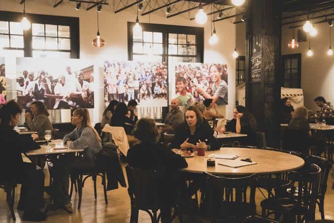 Interior del local con personas reunidas en mesas y decoración con fotografías en las paredes