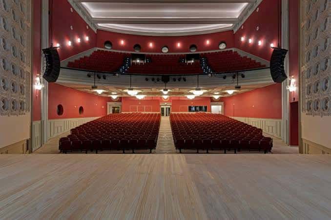 Interior del Teatro Albéniz con butacas rojas dispuestas en gradas y un escenario amplio, ideal para eventos culturales