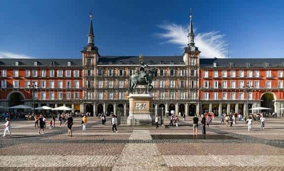 Vista panorámica de la Plaza Mayor de Madrid con la estatua ecuestre de Felipe III al centro y fachadas rojas bajo cielo azul
