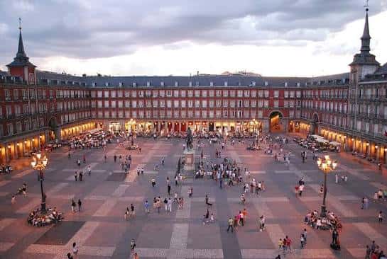 Plaza Mayor de Madrid al atardecer, iluminada con farolas y multitud de visitantes caminando por el empedrado