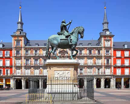 Primer plano de la estatua ecuestre de Felipe III en la Plaza Mayor, con las torres y fachadas rojas al fondo
