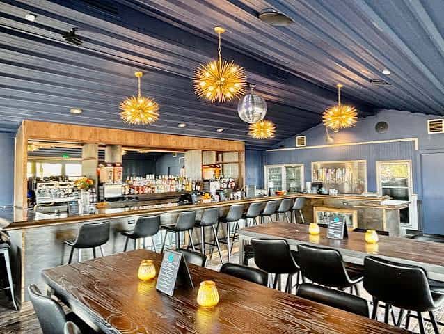 Bar principal con iluminación decorativa, barra larga y mesas de madera