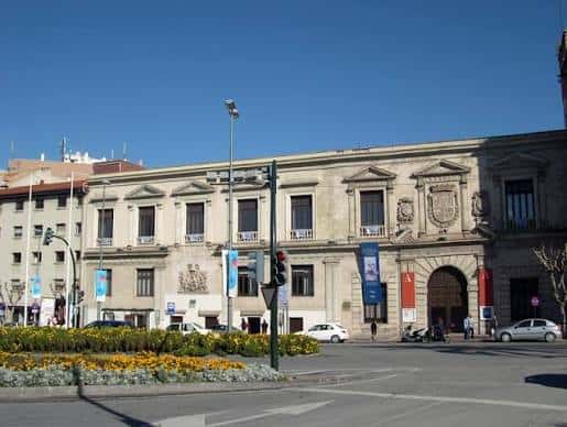 Vista general del Palacio Almudí desde la plaza con tráfico y jardines en primer plano