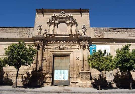 Fachada del Palacio Riquelme con entrada principal y árboles a los lados