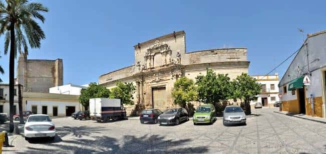 Vista panorámica del Palacio Riquelme desde la plaza con vehículos y palmeras