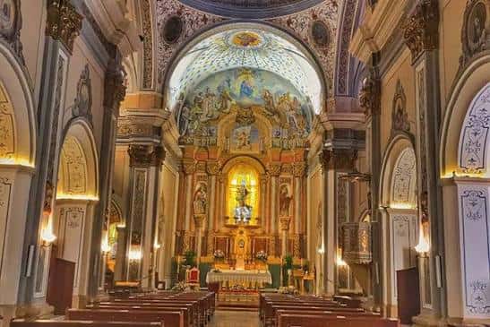 Interior de la iglesia con altar mayor decorado, bóveda pintada y bancos de madera iluminados