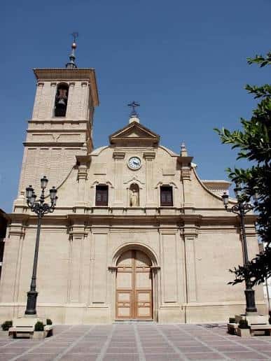 Vista frontal de la Iglesia de Nuestra Señora de la Asunción con fachada de piedra y campanario bajo cielo despejado