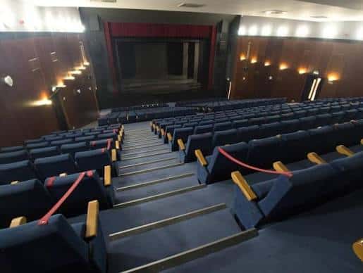 Interior del auditorio con butacas azules y escenario con telón rojo