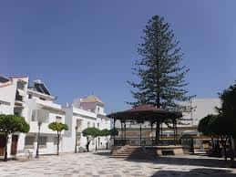 Vista amplia de la plaza con kiosco, árboles y edificios blancos bajo cielo despejado