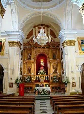 Interior de la iglesia con altar principal, retablo dorado, candelabro y bancos de madera