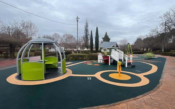 Zona de juegos infantiles con estructuras verdes y suelo de caucho en el Parque de Adoratrices