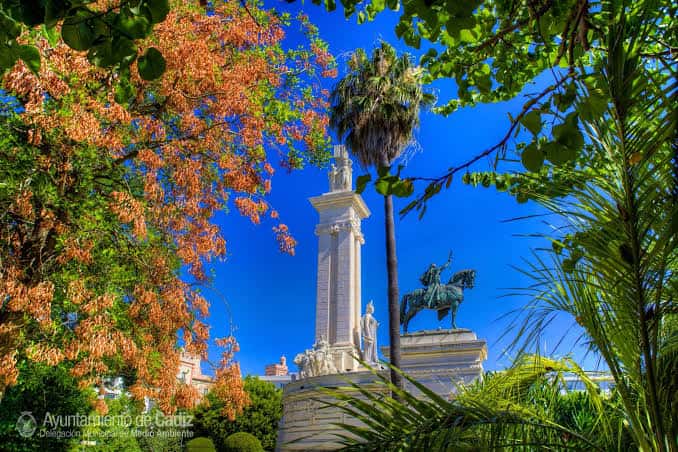 Vista artística del monumento enmarcado por palmeras y follaje de otoño con cielo azul intenso