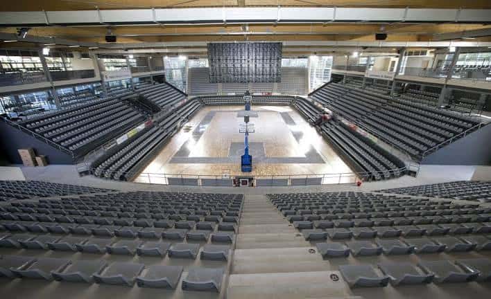 Interior del pabellón con gradas vacías y pista de baloncesto bajo iluminación natural