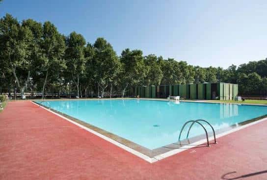 Vista panorámica de la piscina de la Devesa con césped y árboles al fondo