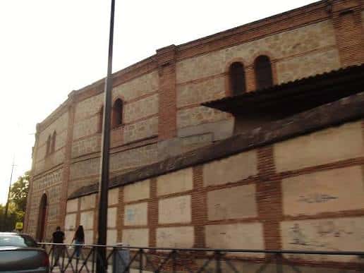 Detalle lateral de la Plaza de Toros La Caprichosa, con muros de piedra y ladrillo, ventanas arqueadas y estructura histórica visible