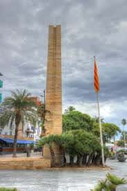 Monumento a Francesc Macià en plaza urbana con cielo nublado y vegetación alrededor