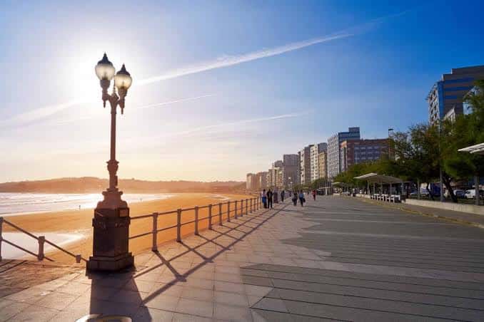 Paseo marítimo de la Playa de San Lorenzo al atardecer con farolas y edificios al fondo