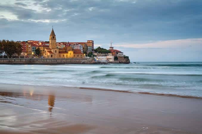 Vista panorámica de la Playa de San Lorenzo con la iglesia de San Pedro iluminada al atardecer