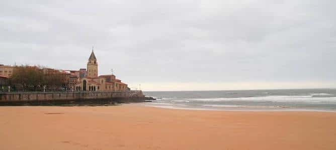 Playa de San Lorenzo en un día nublado con la iglesia de San Pedro al fondo