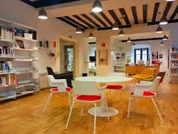 Interior moderno de la biblioteca con mesas redondas, sillas blancas y rojas, estanterías y techos de vigas de madera