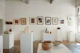 Interior de la galería con cerámicas y cuadros en exhibición sobre pedestales blancos