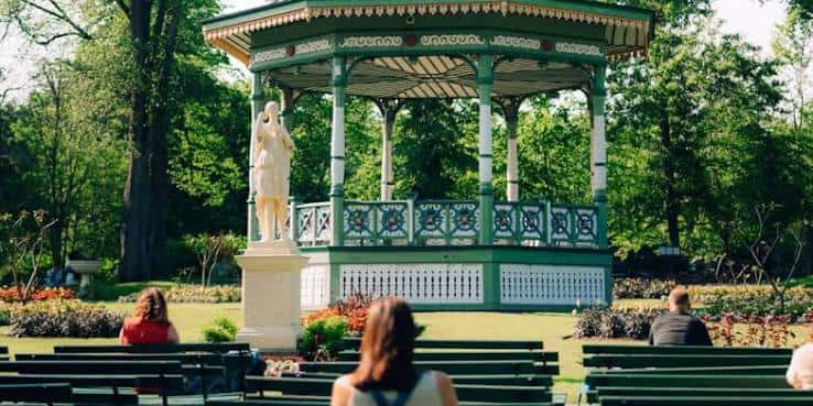 Vista del kiosco de música verde y blanco con una estatua en primer plano