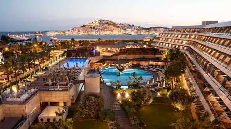 Vista panorámica nocturna del Ibiza Gran Hotel con piscinas iluminadas y la ciudadela de Ibiza al fondo