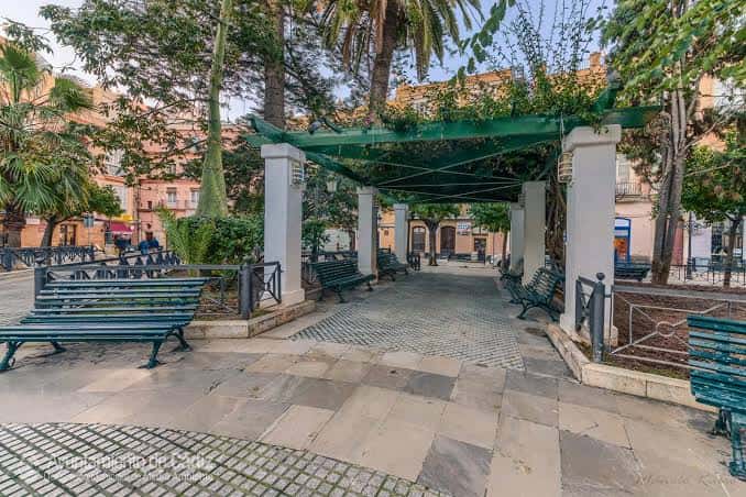 Pérgola con bancos y vegetación en un rincón de la plaza