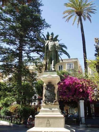 Estatua de un personaje histórico en el centro de la plaza rodeada de palmeras y flores